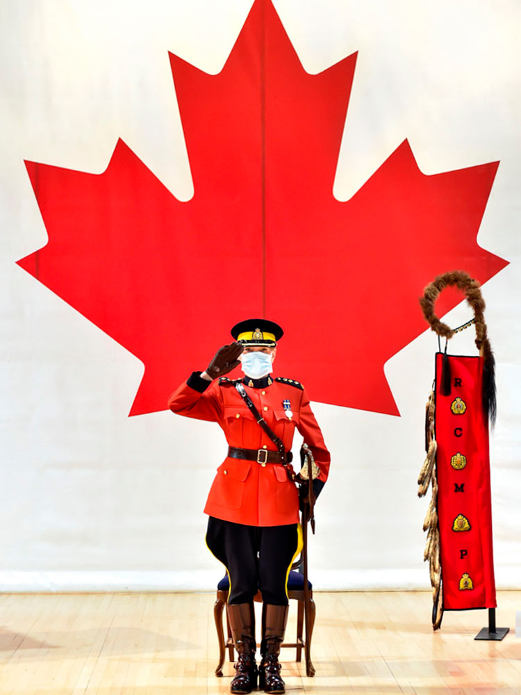 Chief Superintendent Sylvie Bourassa-Muise, Commanding Officer of Depot Division, salutes in front of the Canadian Flag and an Eagle Staff