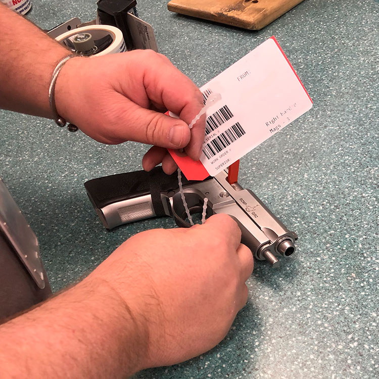 A person attaches an identification tag through the trigger guard of an RCMP-issued pistol.