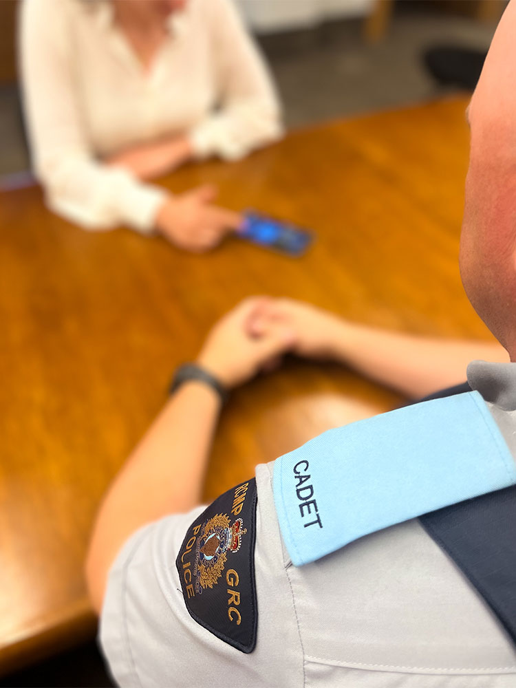 A cadet looks at a phone with an individual at a table.