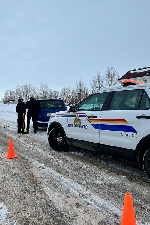 An RCMP officer offers support to a client. A police car can be seen by a blue van.