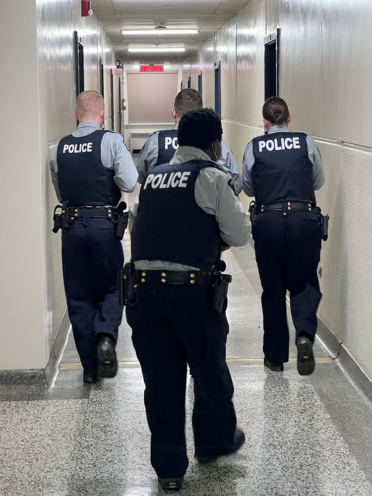 Four cadets walk down a hall in tactical formation.