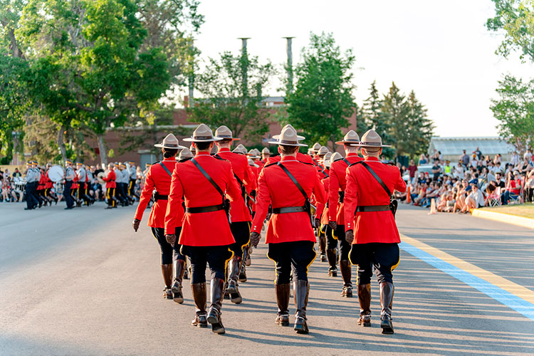 Cadets in red serge march. A crowd can be seen in the distance.