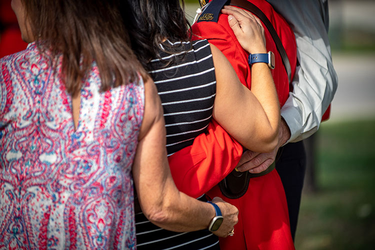 A family wraps arms around each other and one wears a red serge.