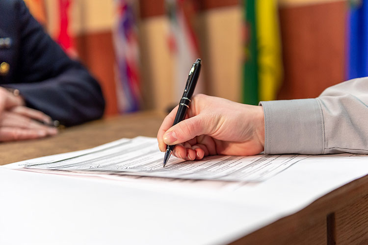 An individual in a grey shirt signs a document with a pen.