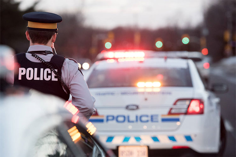 An RCMP officer at a traffic stop. He is behind a police vehicle with its emergency lights activated.