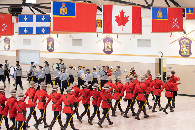 Cadets in red serge and blues march. Some cadets have music instruments.