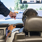 An instructor is pointing at the screen that the cadet is looking at while using the driving simulator.