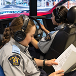 Two cadets use a driving simulator. One is reading instructions while the other is driving.