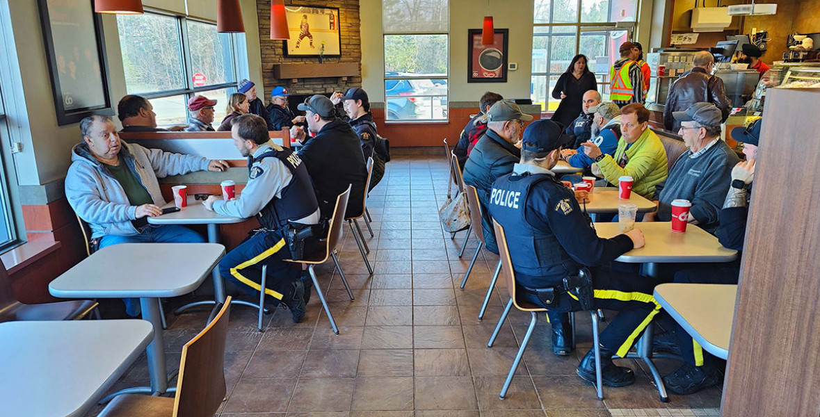 Uniformed RCMP officers and civilians are seen sitting down at tables in a Tim Horton's