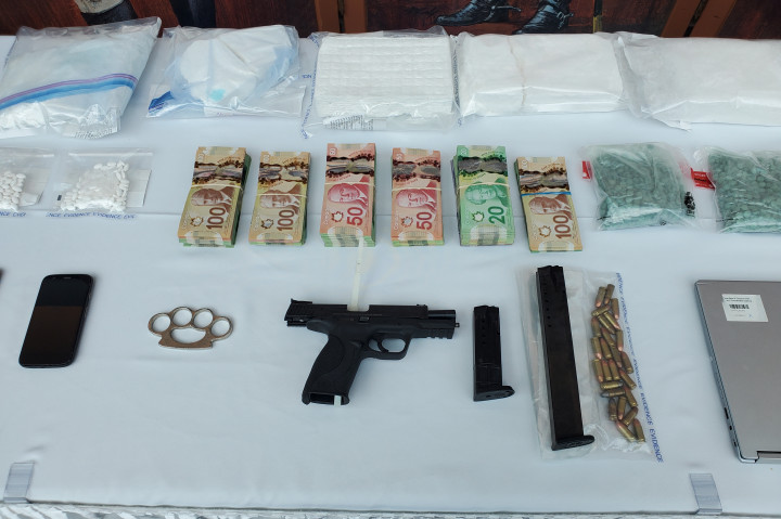 Weapons, money, and illicit drugs can be seen on a white table.