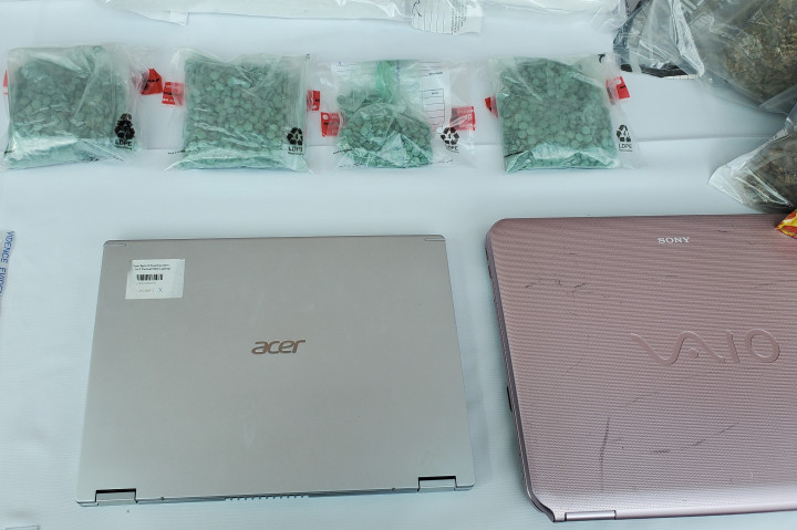 A variety of illicit drugs and two laptops can be seen on a white table.