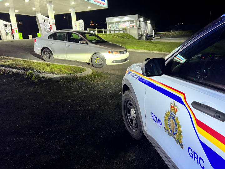 An RCMP cruisier is parked in front of a white car, blocking its exit from a gas station. 