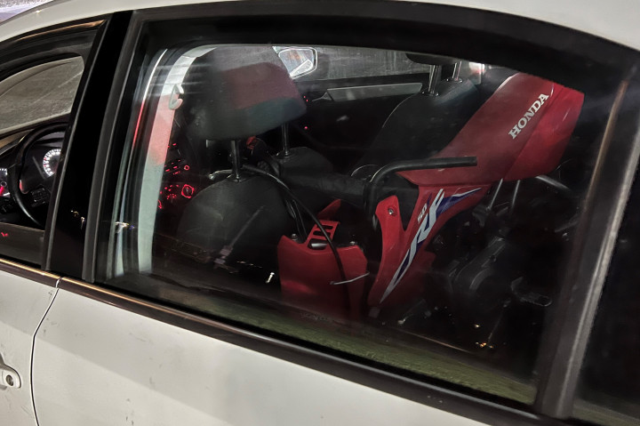 A photo through the backseat window of a car, showing a small red Honda dirt bike inside. 