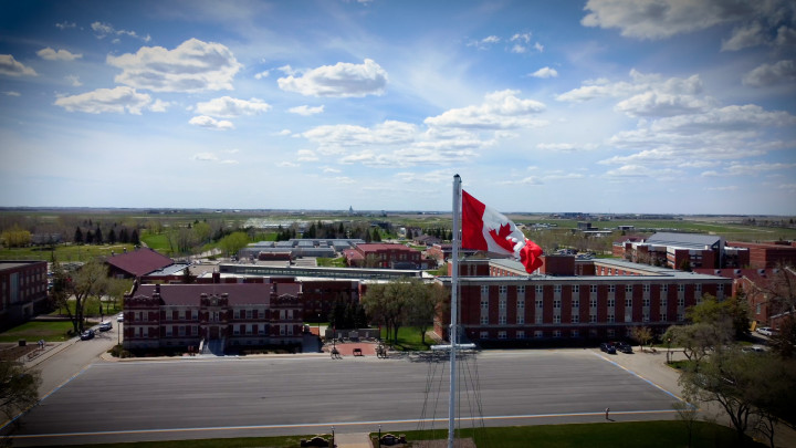 Le drapeau du Canada à l'École de la GRC avec la Cour d'honneur et des bâtiments en brique en arrière-plan.