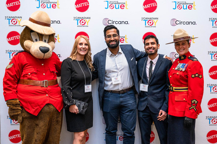 The RCMP Safety Bear and Cpl. Angelique Dignard pose in front of a sponsor backdrop, with three representatives from Mattel Canada Inc.