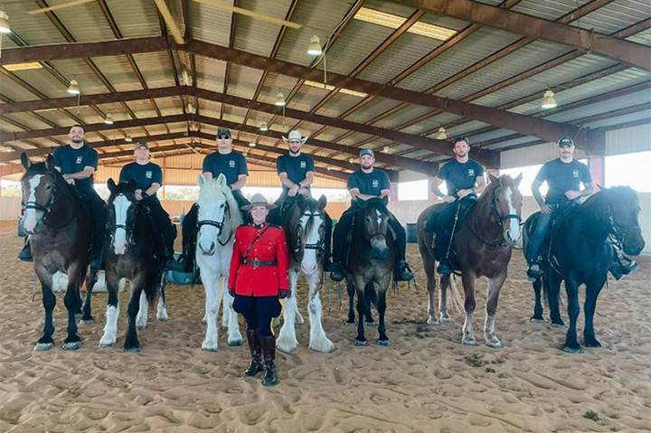 La caporale Marie-Michèle Ouimet prend la pose devant sept chevaux et leurs cavaliers aux écuries de l'Austin Mounted Police.