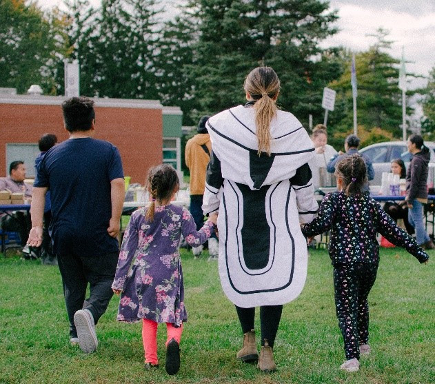 Une femme de la communauté inuit portant un vêtement traditionnel appelé Amauti. Elle tient par la main trois enfants qui marchent en faisant dos à la caméra.