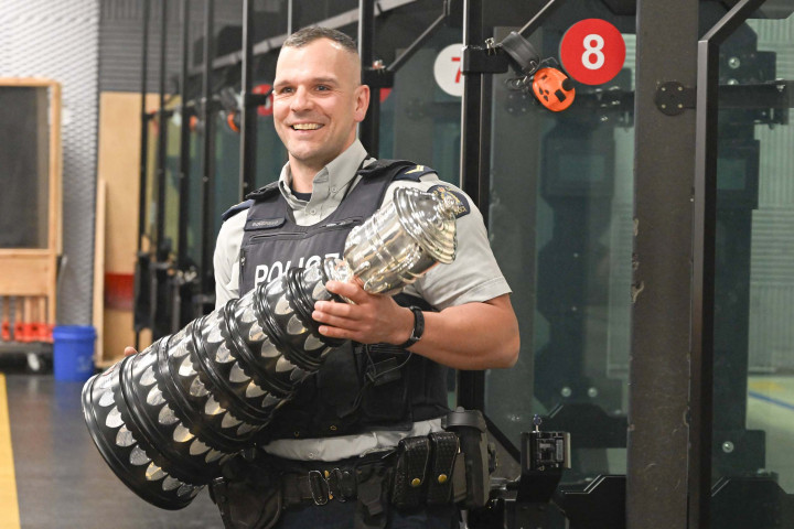 An RCMP police officer smiles as he holds up a large trophy.