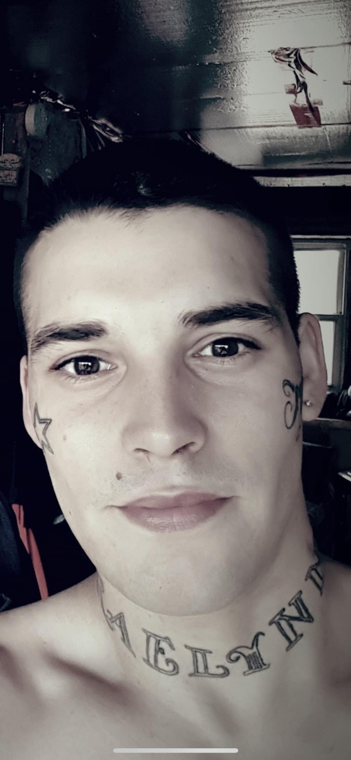 Head shot of a man with short dark hair and tattoos on his face and neck.