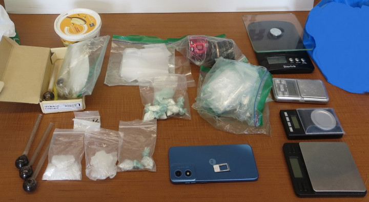 A number of items are displayed on a wooden surface including zip lock bags of various drugs, a cell phone, four digital scales and drug paraphernalia.