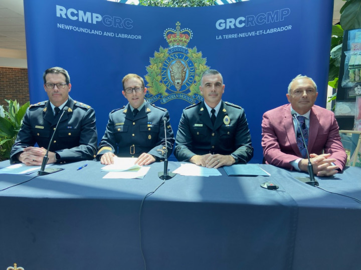 A group of three uniformed police officers and a man in a suit sit at a table to give a news conference. 