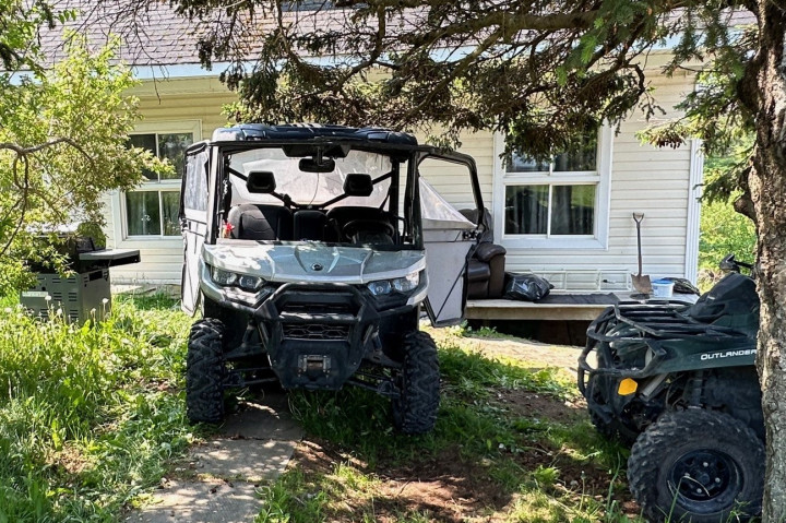 A UTV (side by side) is seen in front of a house. The front end of an ATV can also be seen parked nearby next to a tree.