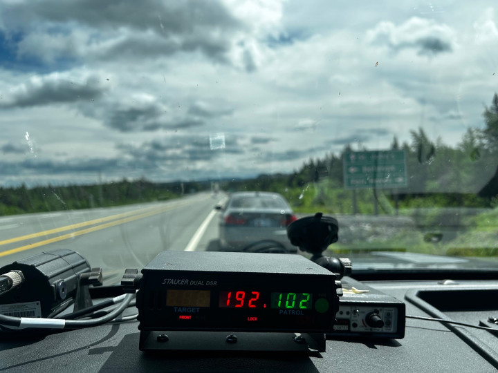 Un radar sur le tableau de bord d'un véhicule de police affiche une vitesse de 192 km/h. Un véhicule est immobilisé devant un véhicule de police par une journée nuageuse.
