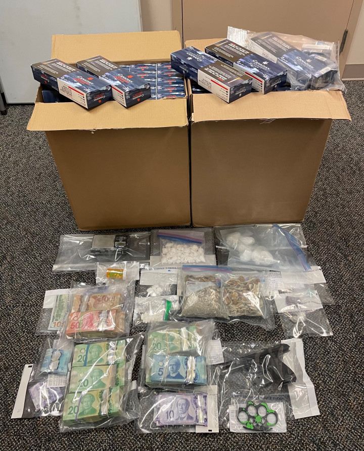 Photo of seized items including approximately 310 grams of cocaine, approximately 170 grams of psilocybin, approximately 41 grams of MDMA, more than 17,000 illegal cigarettes, a handgun and a loaded clip, drug trafficking paraphernalia, and a large sum of cash.