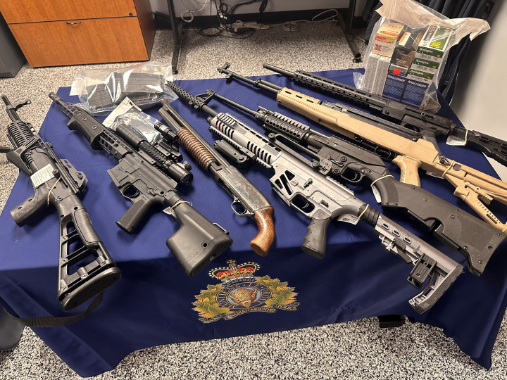 Sept armes à feu, une quantité de tabac de contrebande et une quantité de psilocybine disposées sur une table recouverte d'une nappe bleue sur laquelle figure l'écusson de la GRC.