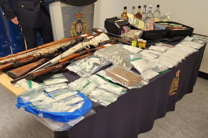 A display of items seized such as guns, cash, drugs and other items consistent with drug trafficking is displayed on a table.