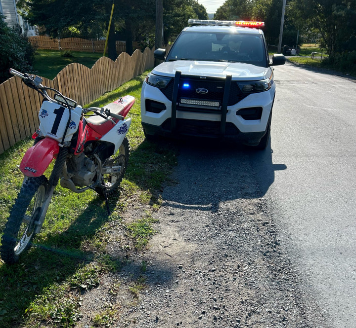 A police cruiser is seen parked behind a dirt bike near the side of a roadway.