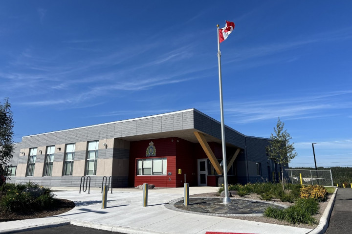 A Canadian flag mounted on a flag pole is pictured in front of a RCMP Detachment.