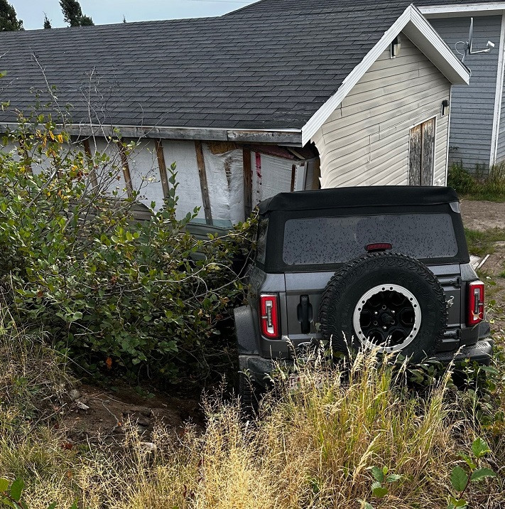 A grey Ford Bronco rests up against a residential shed after a collision.