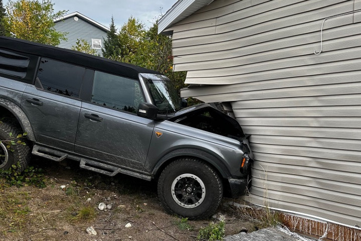 A grey Ford Bronco rests up against a residential shed after a collision.