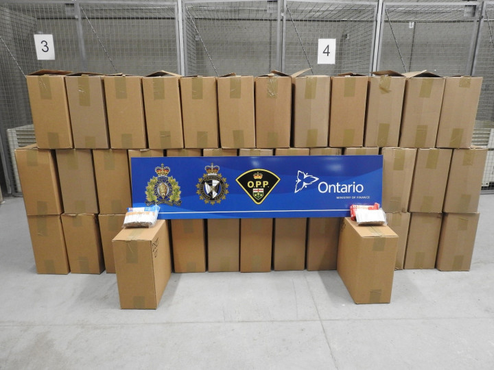 Photo de 40 boîtes de cigarettes non estampillées retrouvées après l'interception d'un véhicule suspect et une enquête plus approfondie du Groupe de travail régional de Cornwall. Sur les boîtes, on a posé un panneau bleu sur lequel figurent les armoiries de la GRC, de l'ASFC et de la Police provinciale de l'Ontario ainsi que le logo du ministère des Finances de l'Ontario.