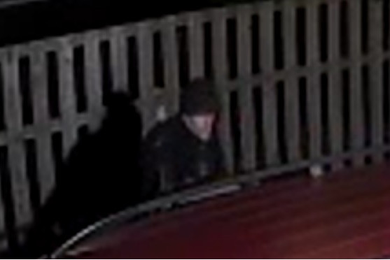 Suspect is seen wearing a black hoodie near a fence.