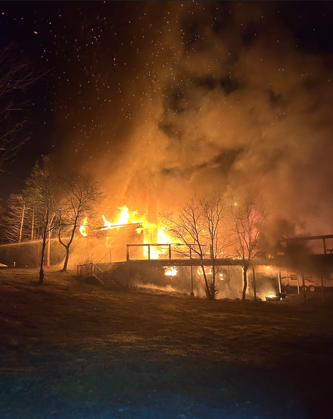 A cabin and trees on fire at night.